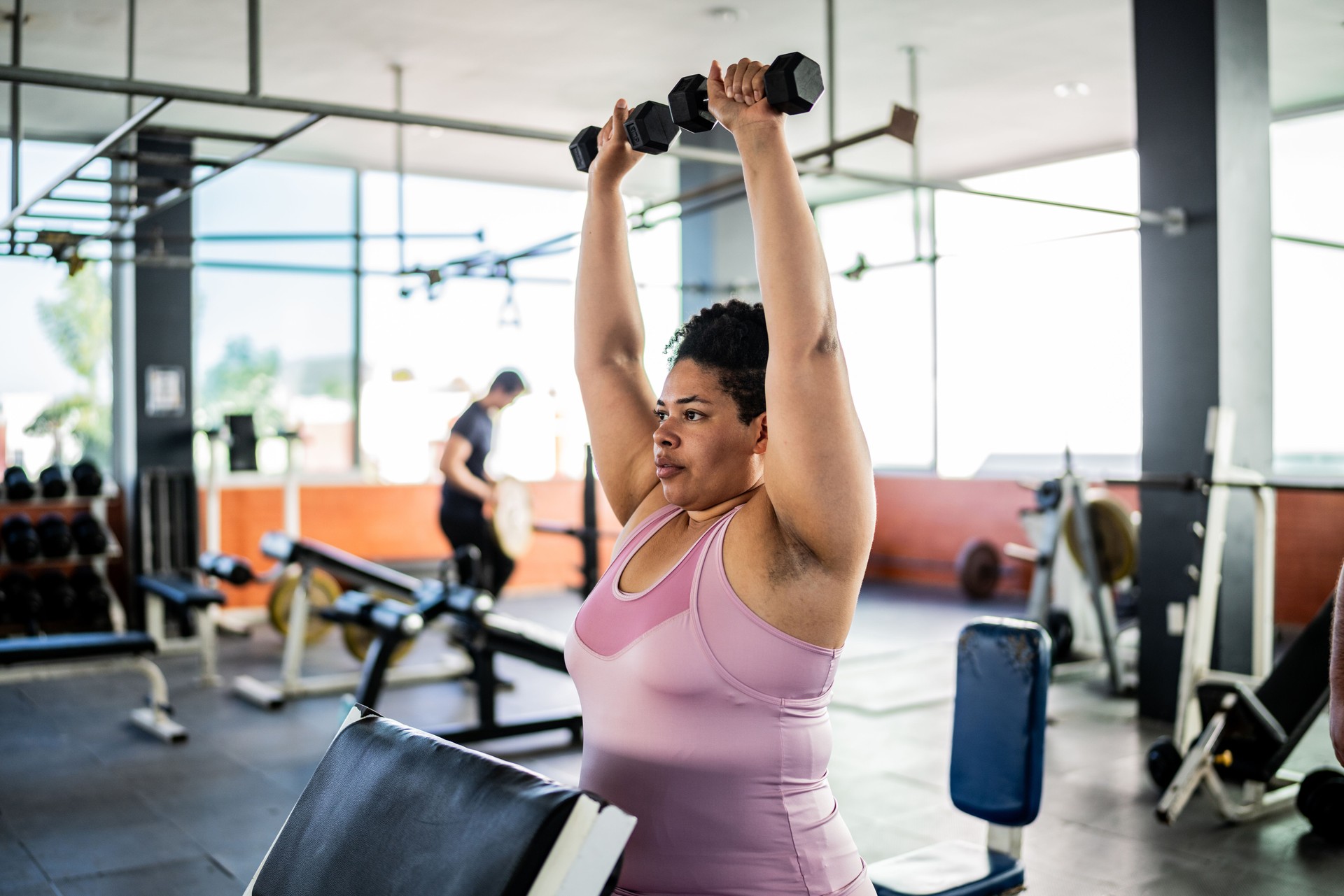 Mid adult woman doing shoulder exercise with dumbbell at gym Mid adult woman doing shoulder exercise with dumbbell at gym